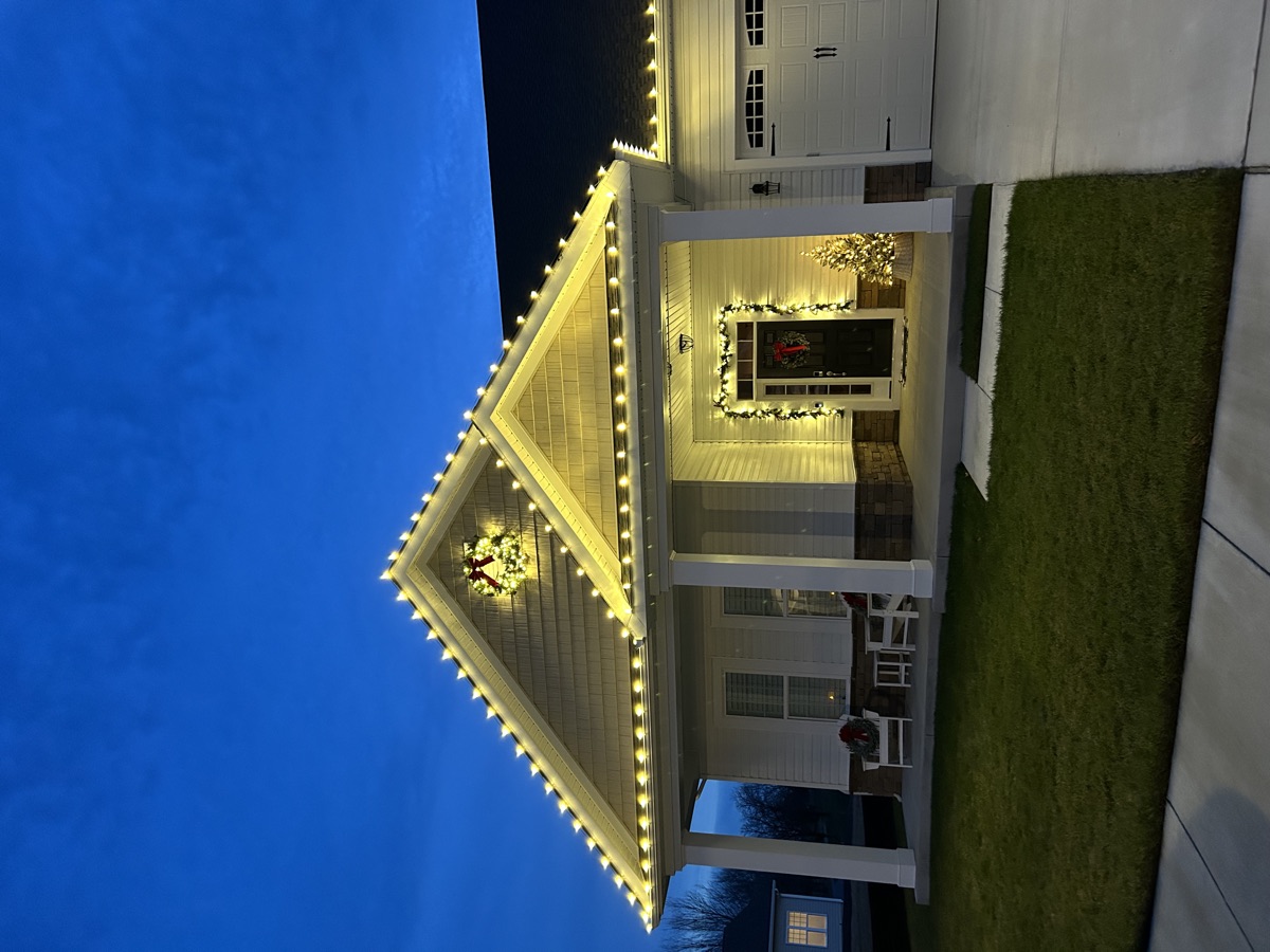 Warm white Christmas bulbs along the gables of a single-story house with a lit wreath